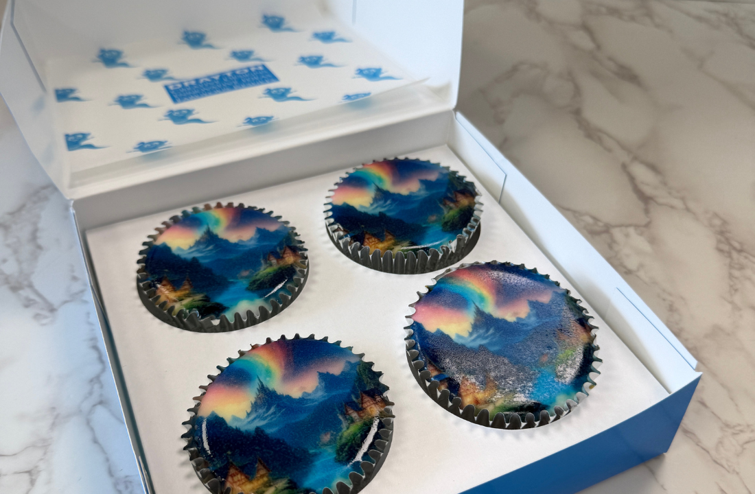 Box of branded cupcakes with colourful printed designs for a corporate event.